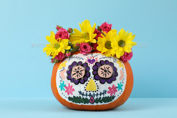 Pumpkin with catrina skull makeup and flowers on blue background