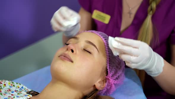 Cosmetologist cleans the skin of a woman's face before a cosmetic procedure alt