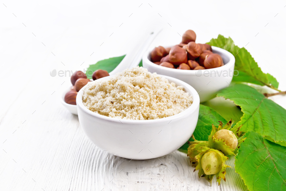 Flour and hazelnuts in bowls on white board - Stock Photo - Images