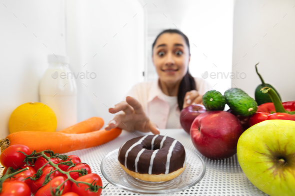 Excited funny woman reaching and taking yummy donut from fridge