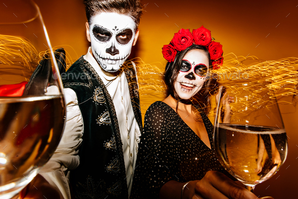 Funny european friends in muertos costume drinking wine. Amazing young people in zombie costumes ce