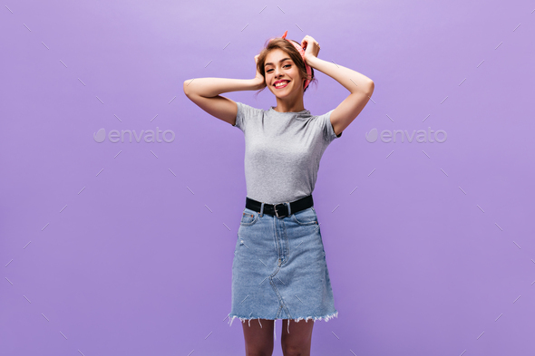 Charming lady in denim skirt and shirt smiling. Pretty woman in pink headband and modern clothes po