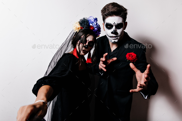 Woman with crown of flowers in black veil makes selfie with her man in frightening halloween costum