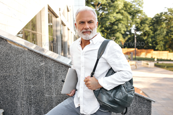 Portrait of bearded man in white shirt outside. White-haired handsome adult in stylish light clothe