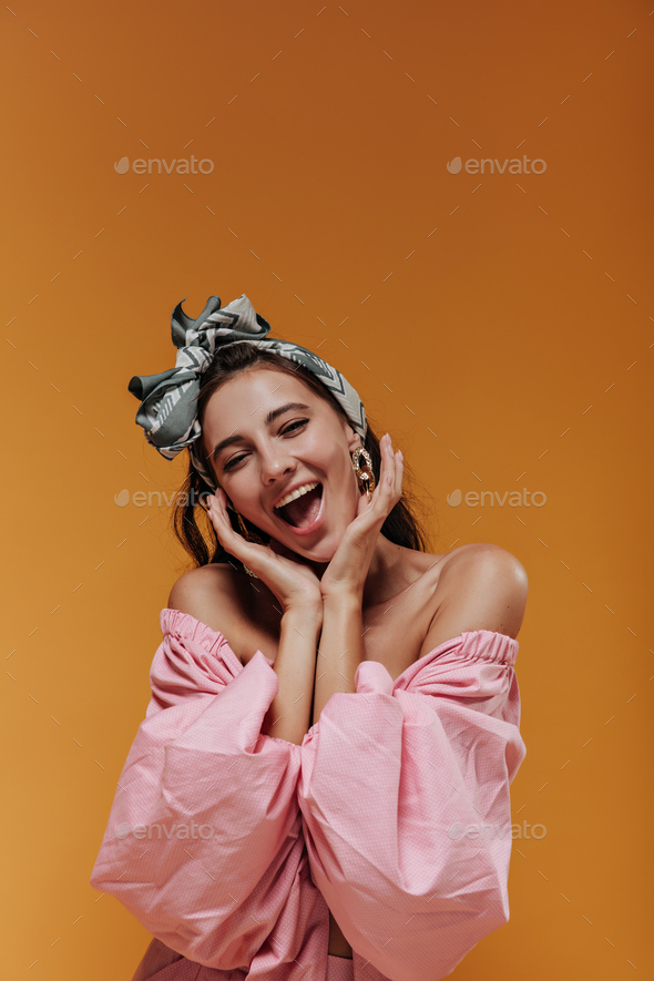 Fashionable cute woman with green stylish bandana and earrings in pink modern blouse looking into c