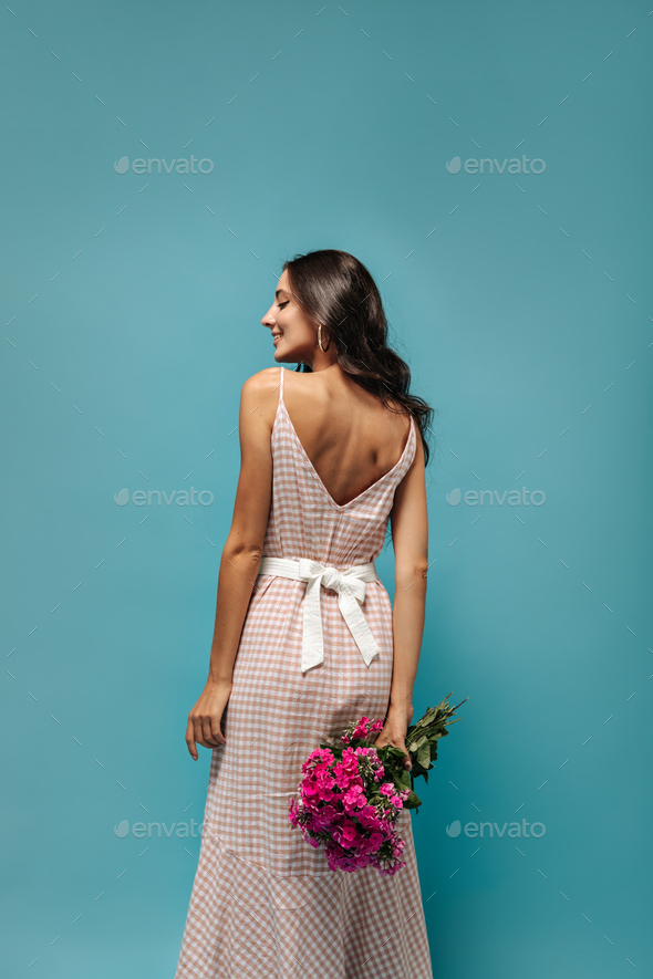 Charming lady in fashionable plaid long dress with white wide belt posing with pink bouquet and smi