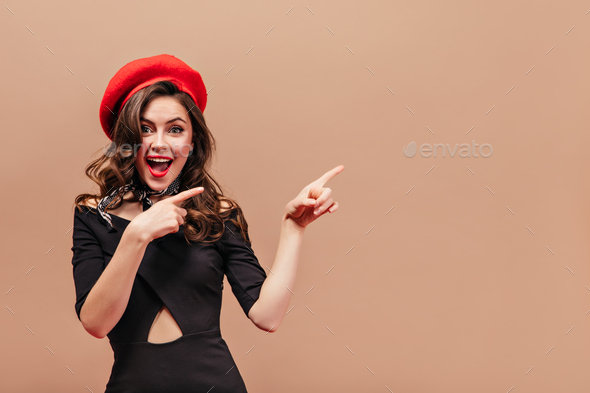 Beautiful girl with wavy hair smiles and points with her fingers to right. Portrait of woman in red