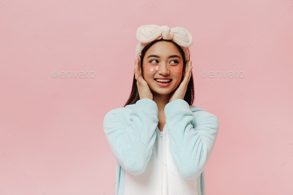 Cute charming girl in blue sleep wear and headband touches her face gently. Pretty women in pajamas