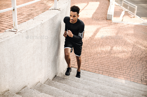 Charming strong active dark-skinned man in black long-sleeved t-shirt and shorts running upstairs a
