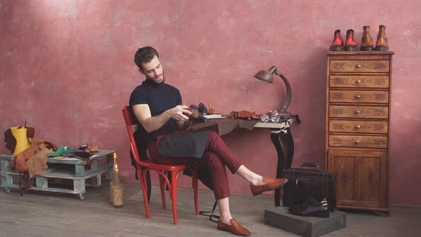 Young Man Cleaning Leather Boots While Sitting on Chair alt
