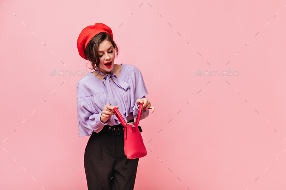 Beautiful woman wearing red beret, blouse and black pants peeks into open bag