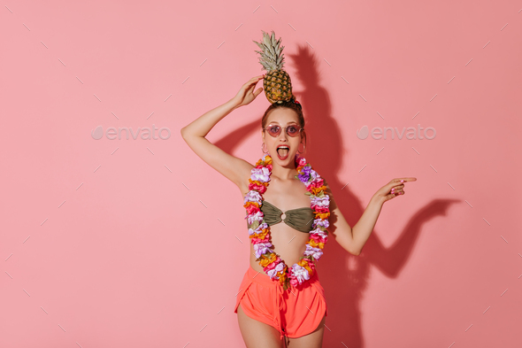 Surprised lady in khaki trendy swimsuit, pink shorts and charming necklace of flowers holding on he