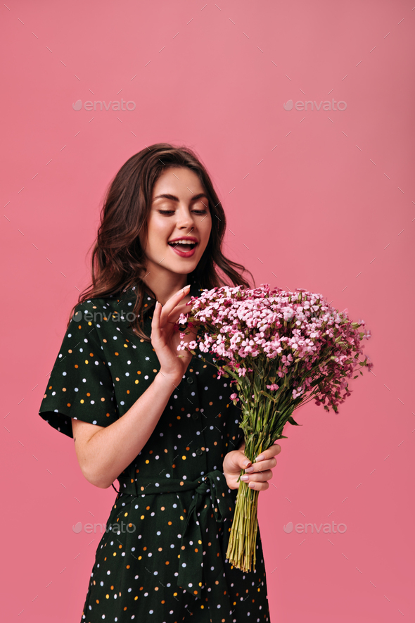 Pretty woman in dark green dress looks at her pink bouquet. Lady in dark  clothes enjoys beautiful a Stock Photo by look_studio