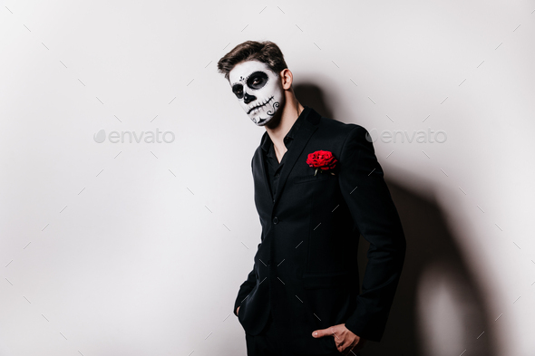 Guy in black suit with red rose in his pocket looks into camera