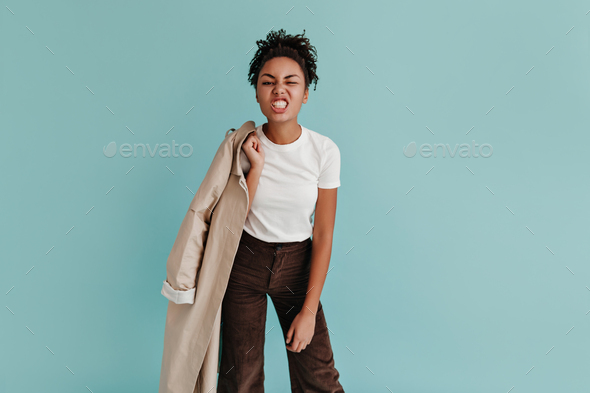 Happy black lady holding trench coat and laughing. Studio shot of inspired african american girl sm