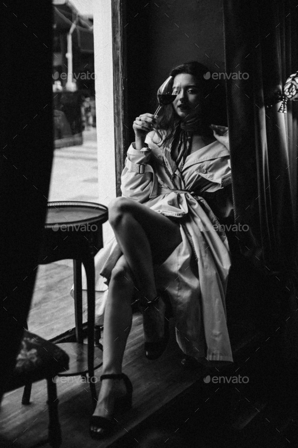 Elegant lady resting in bar with wine glass. Black and white portrait of young beautiful woman dres