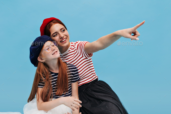 Ginger lady in red beret, striped t-shirt and black trendy skirt shows aside her sister with long h