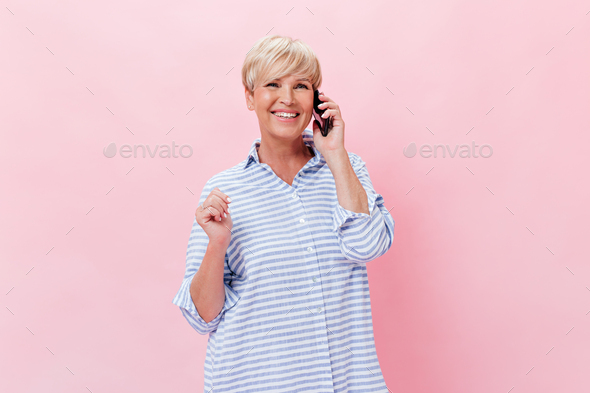 Charming lady in plaid shirt talks on phone and smiles on pink background