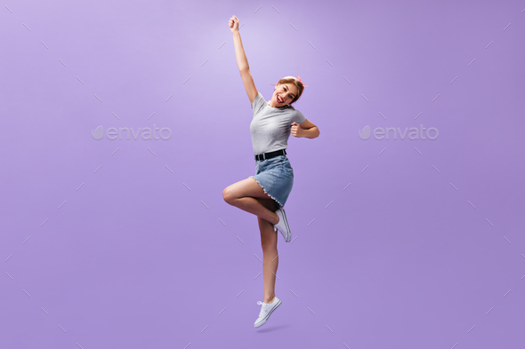Full length shot of woman in denim skirt on purple background. Slim cool girl with pink bandana and