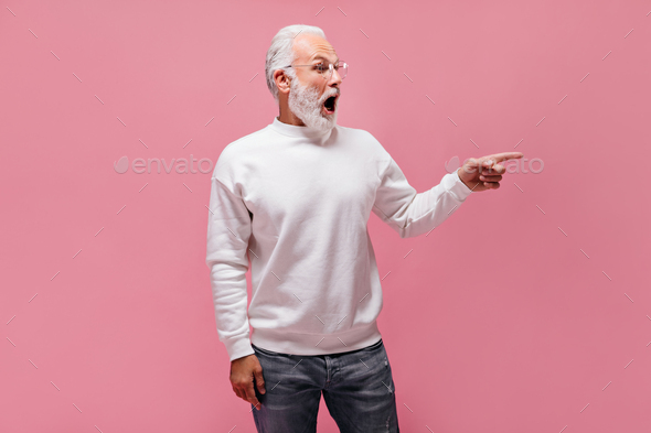 Shocked man in white sweater pointing to place for text. Surprised adult guy in eyeglasses and mode - Stock Photo - Images