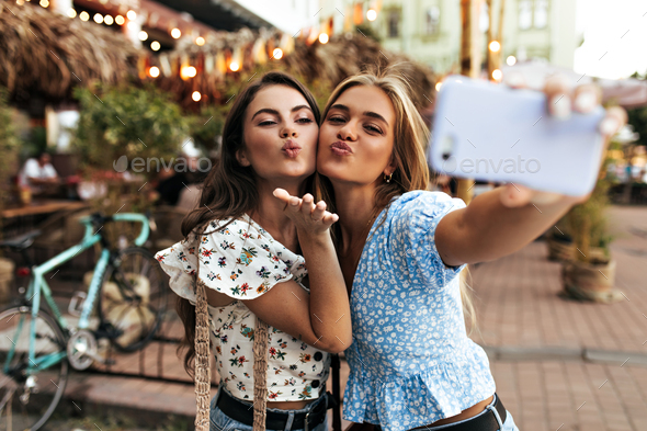 Pretty young attractive girls blow kiss and take selfie in good mood outside. Cheerful woman in blu