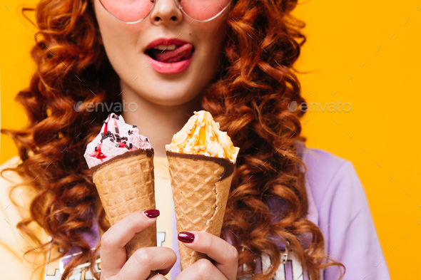 Close-up shot of redhead woman licking her lips. Girl holds ice cream with different toppings