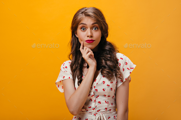 Open eyed woman on cherry printed blouse looks into camera. Fashionable wavy girl with blue eyes in