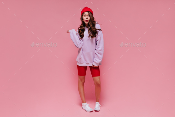 Cool brunette girl in red hat, cycling shorts and purple hoodie whistles. Curly woman with bright l