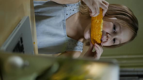 Vertical Screen Girl Eating Boiled Sweet Corn and Looking at Laptop alt