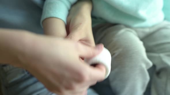 mom bandages a wounded hand to a small child, close-up without faces alt