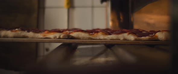 Traditional Al Taglio pepperoni pizza being placed in the hot oven. Slow motion. alt