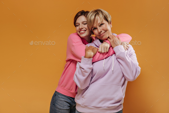 Lovely short haired girl in trendy hoodie and jeans smiling with closed eyes and hugging her mother