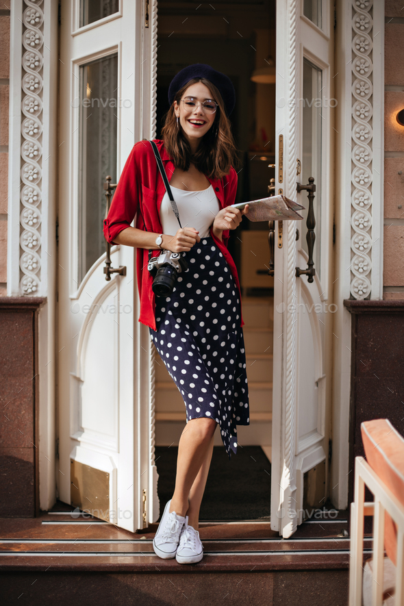 Cheerful young in white top, polka dot skirt, red shirt, beret and stylish accessories, Stock Photo by look_studio