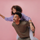 Curly girl jumped on her boyfriends back and showing peace sign. Dark-skinned couple has fun and sm - PhotoDune Item for Sale