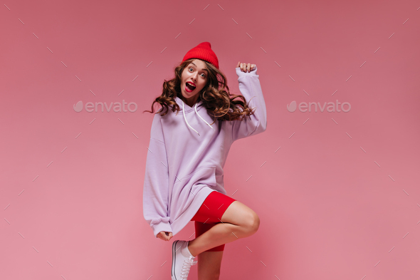 Curly brunette girl in red cycling shorts and purple hoodie jumps on isolated. Cool active woman in