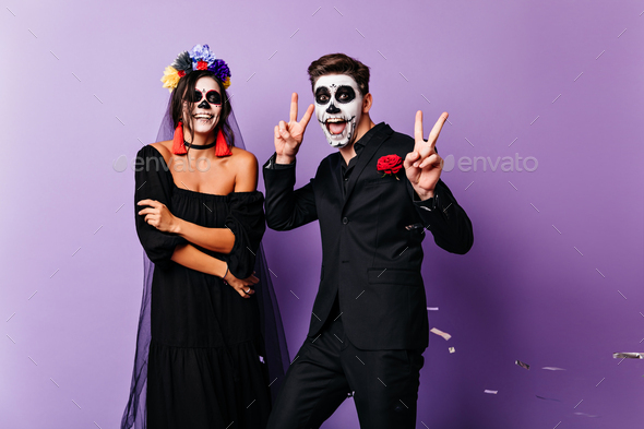Smiling dead bride posing on purple background. Couple of zombies dancing together.