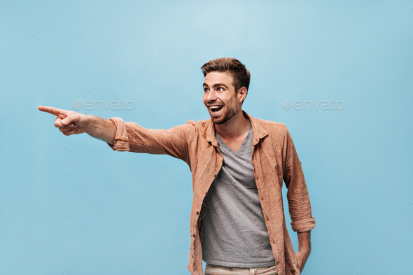 Emotional bearded man in grey cool t-shirt and stylish shirt showing aside is finger and rejoices o - Stock Photo - Images