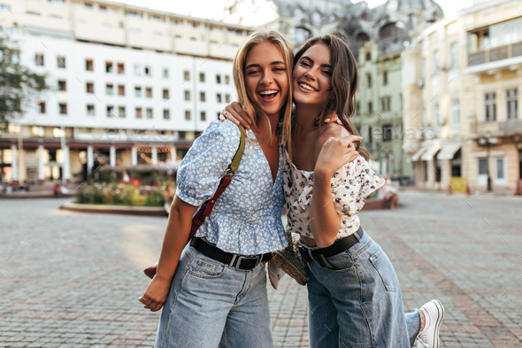 Charming pretty girls in stylish denim pants and floral tops hug