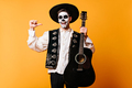 Excited guy in mexican traditional clothes holding guitar. Happy dead singer having fun at hallowee - PhotoDune Item for Sale