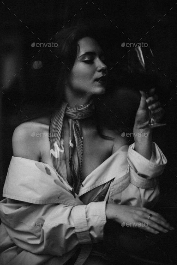 Portrait of attractive lady with wine glass. Black and white photo of young woman in stylish trench