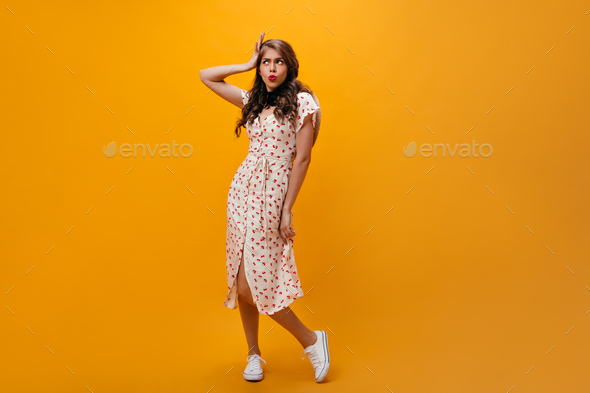 Charming woman in white dress mannerly posing on orange background ...