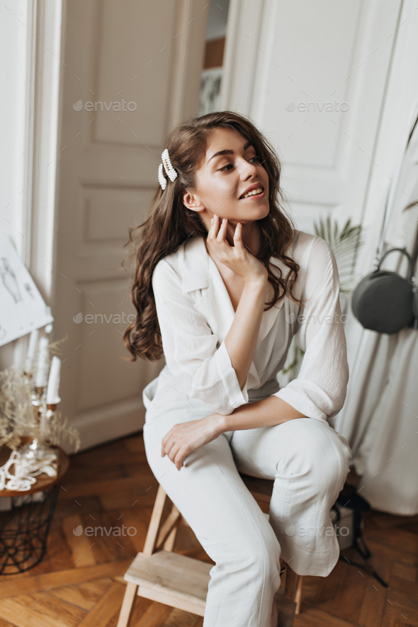 Woman in white suit smiling. Attractive young lady in beige blouse and linen pants sitting on chair