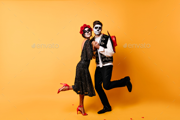 Full-length portrait of funny zombies dancing in studio. Indoor photo of dead couple celebrating ha