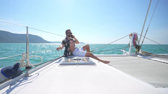 4K Caucasian man talking on phone for corporate business while catamaran sailing on summer vacation.