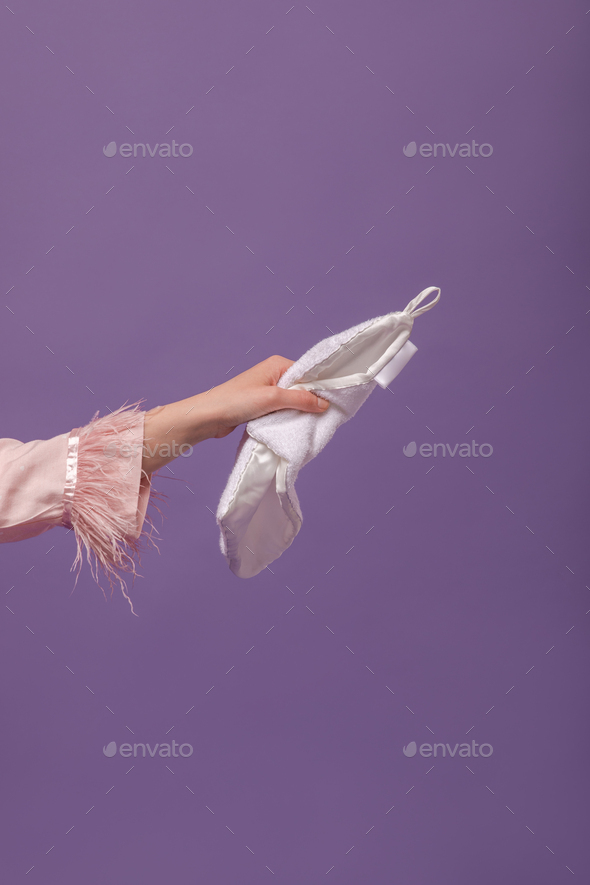 Skincare and wellness concept. Woman hand in pink clothes with feathers holding white silk towel is