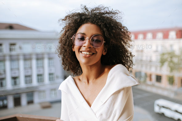 Dark-skinned girl in white clothes and round eyeglasses smiling on ...