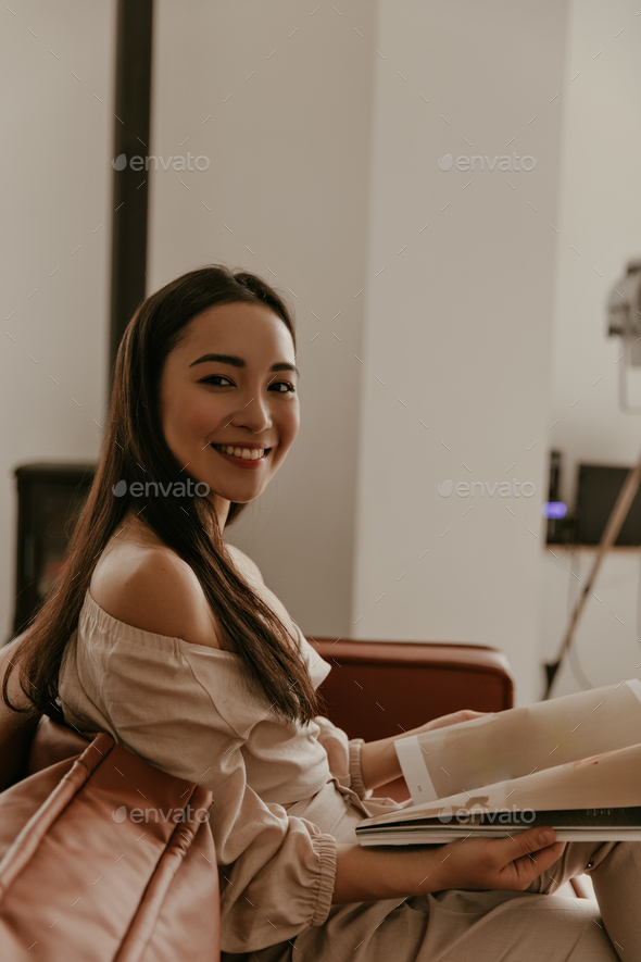 Tanned charming brunette woman in beige blouse and linen pants smiles widely, looks into camera, si