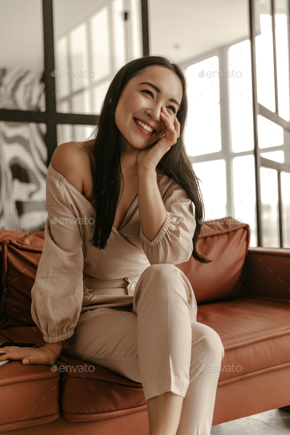 Attractive optimistic brunette Asian woman in trendy beige pants and stylish cropped blouse smiles