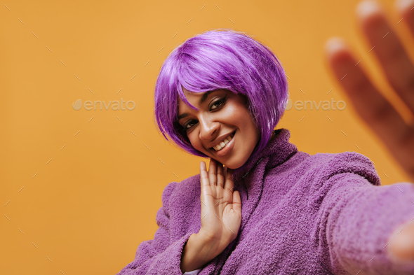 Beautiful woman with short purple hairstyle smiling on isolated background. Bright girl in warm lil