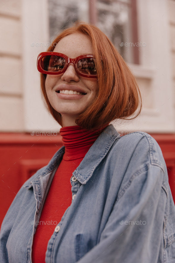 Cheerful young lady posing on street. Cute girl with red hair